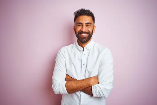 Man with short dark hair and a full beard wearing a long white buttoned shirt with a collar.  The background of the image is pink.  The image is representative of a testimonial for 'h.r. simpl' website but does not represent the person who wrote the testimonial.